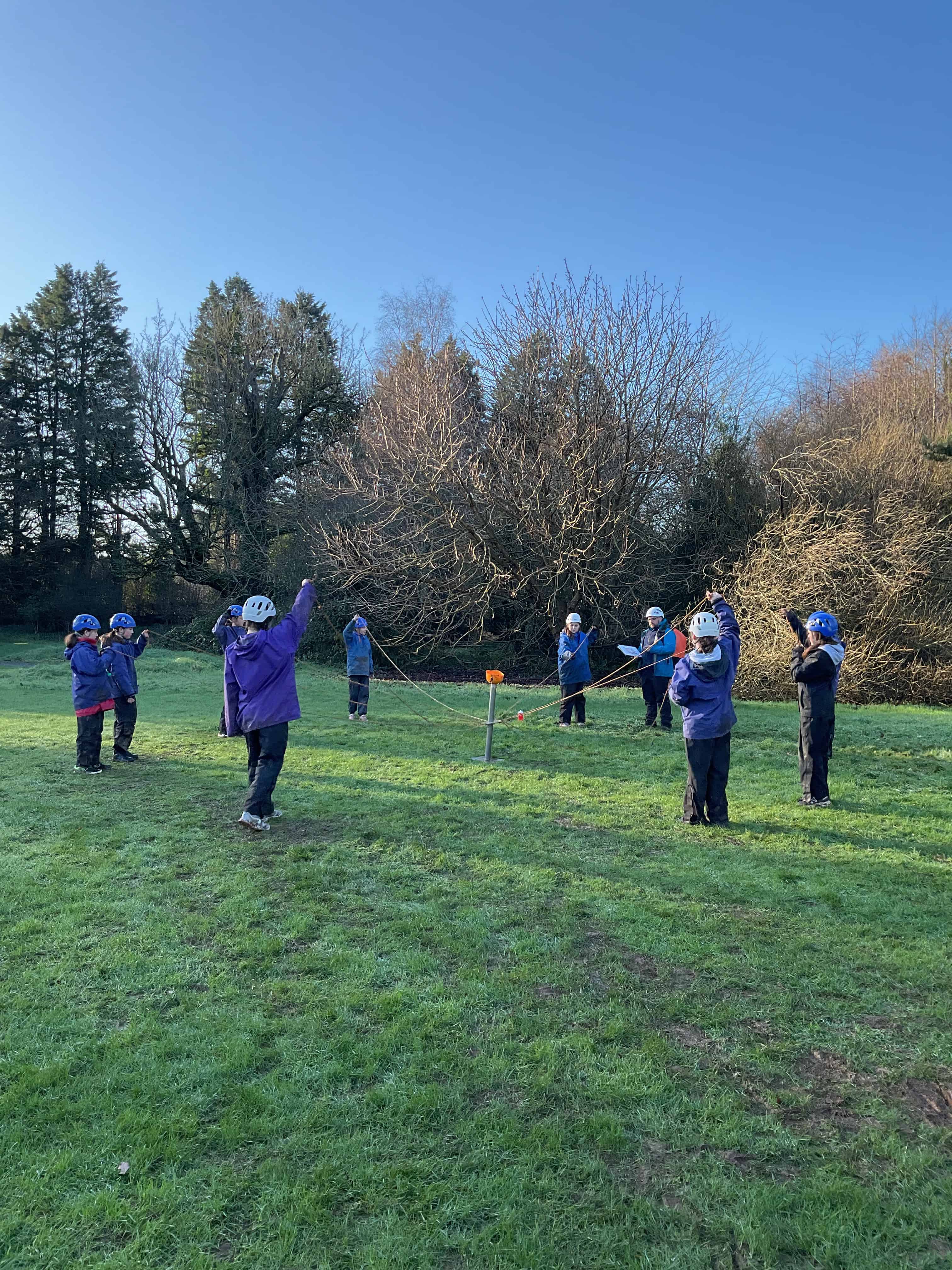 Students from Priestnall School stand in a circle on a field each holding a rope, working together to get an object to a centre point with their ropes.