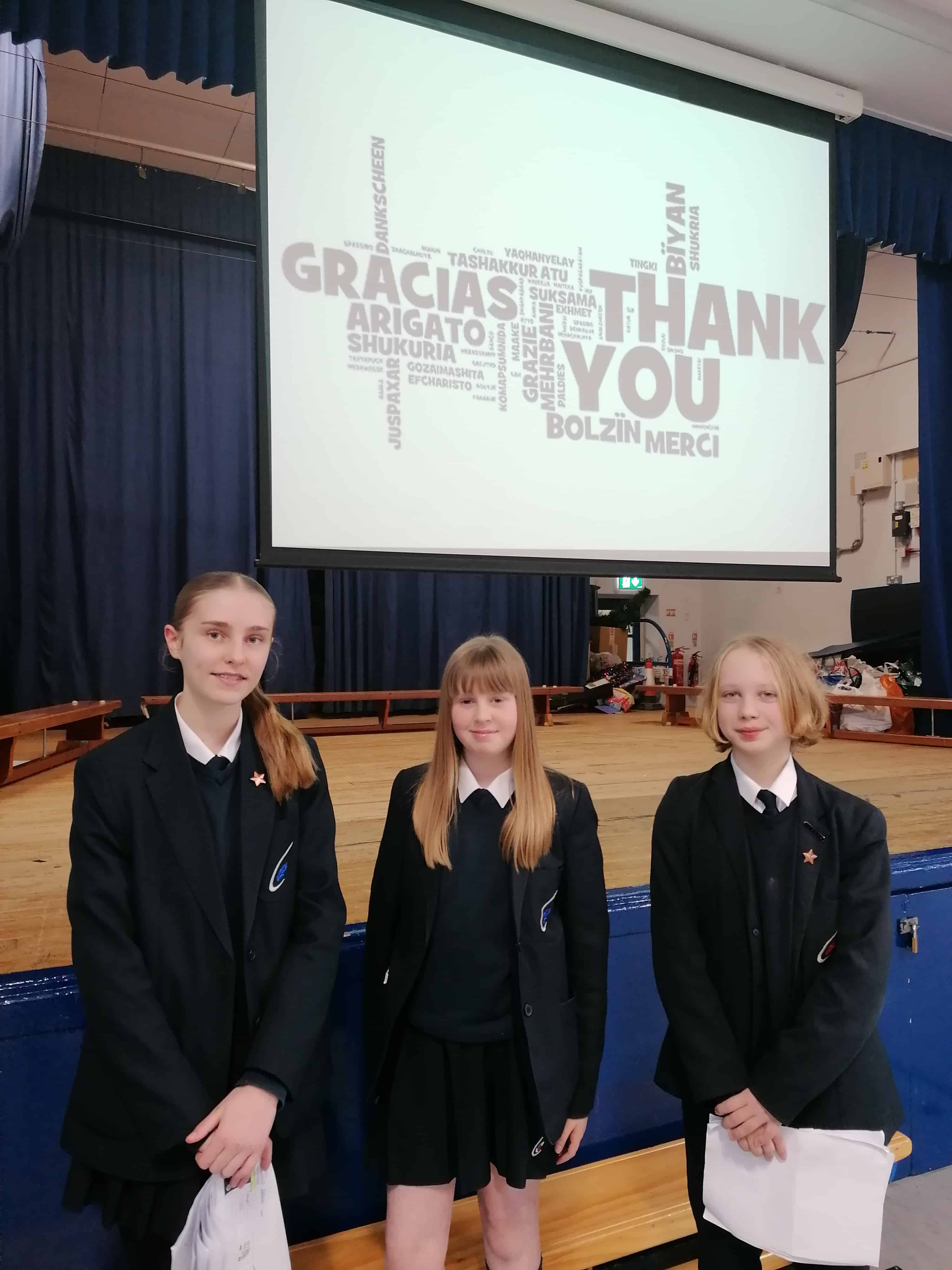 Priestnall School Languages Ambassadors stand in a school hall in front of their Languages presentation.