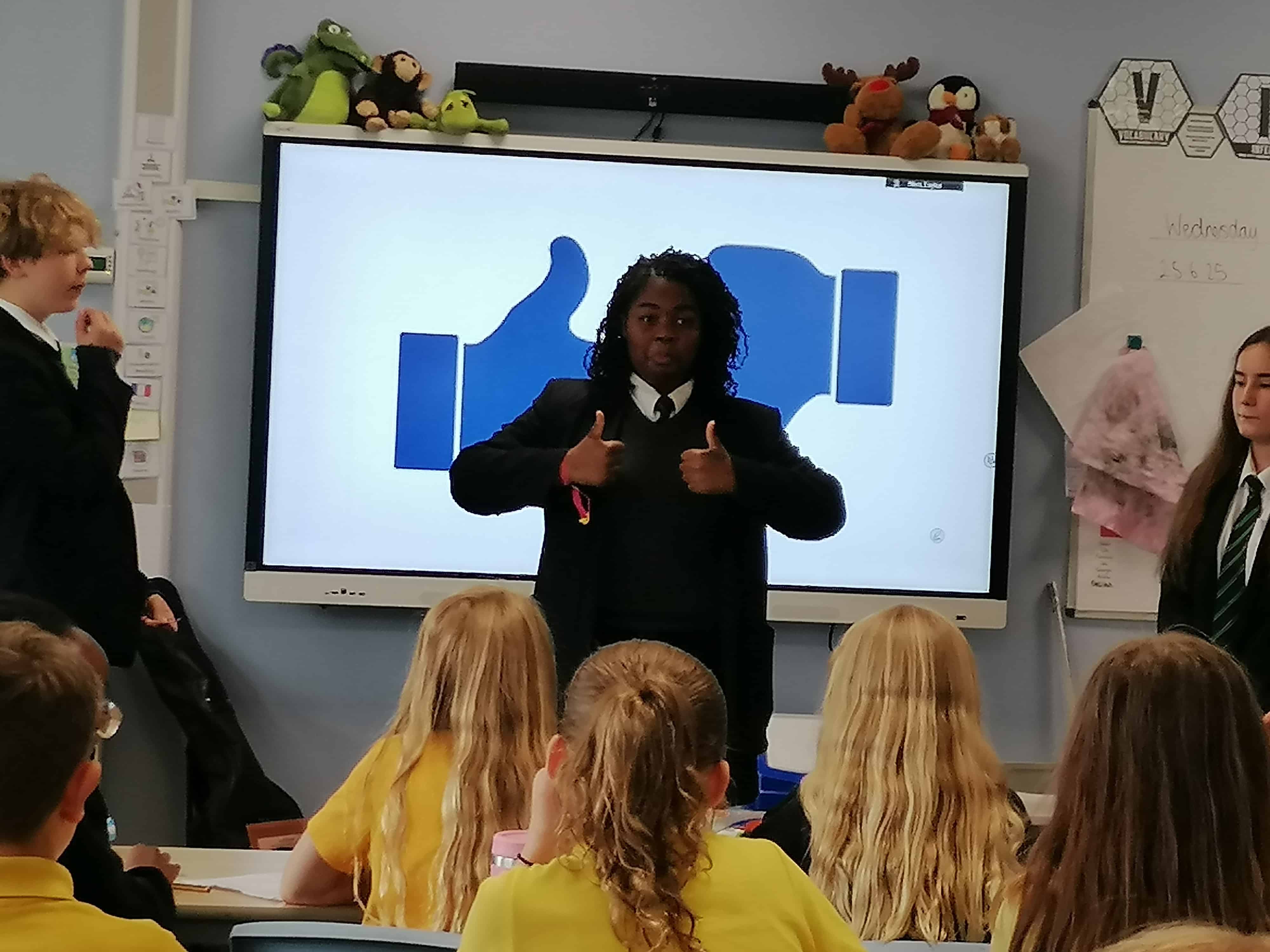 A Languages Ambassador from Priestnall School stands with their thumbs up in a classroom at a primary school