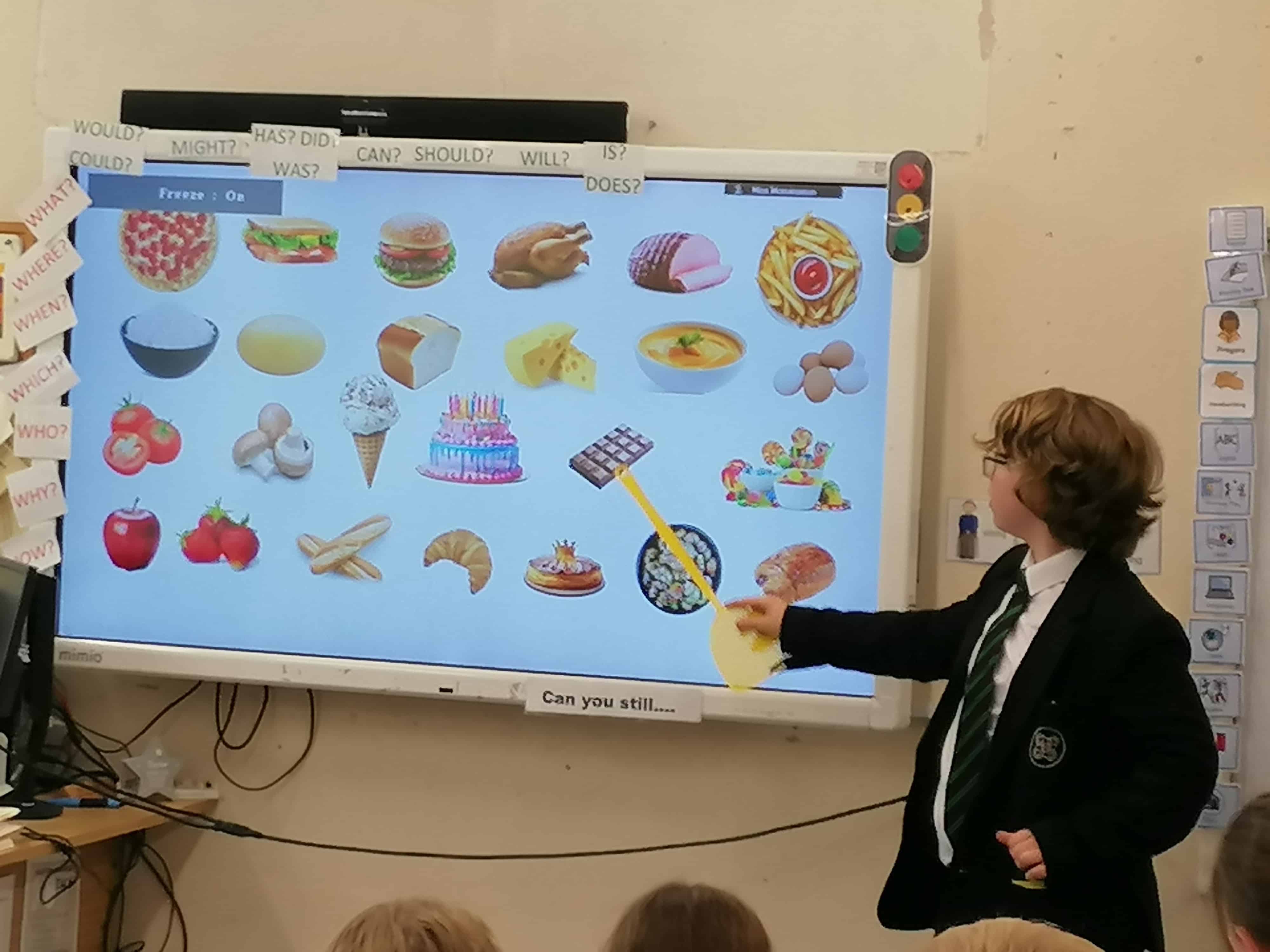 Languages Ambassadors from Priestnall School teach primary school pupils different foods on a smartboard.