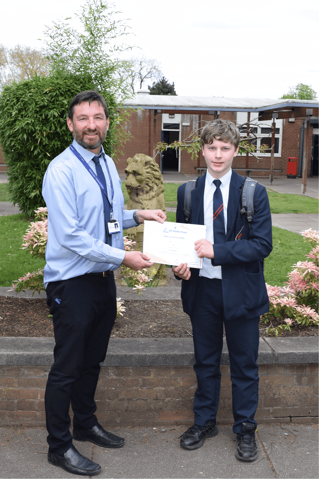 Priestnall School student holds a certificate of merit with a maths teacher after success in UKMT Grey Kangaroo.